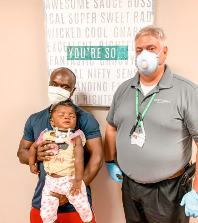 Dad, infant girl, and orthotist posing for picture. unique orthotic case requires innovative solution to keep baby's head up