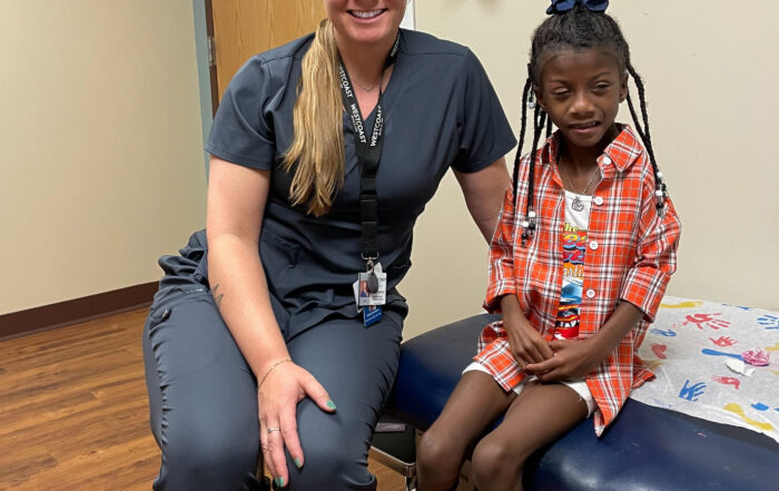adult female with blond hair wearing scrubs sitting on medical bed with young african-american girl wearing bilateral AFO leg braces
