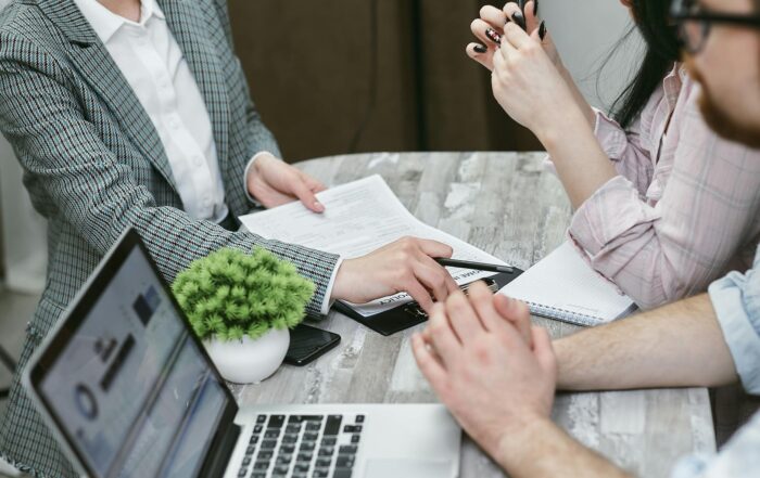 zoomed in image of a desk with laptop and paperwork and hands pointing to paperwork in explanation.